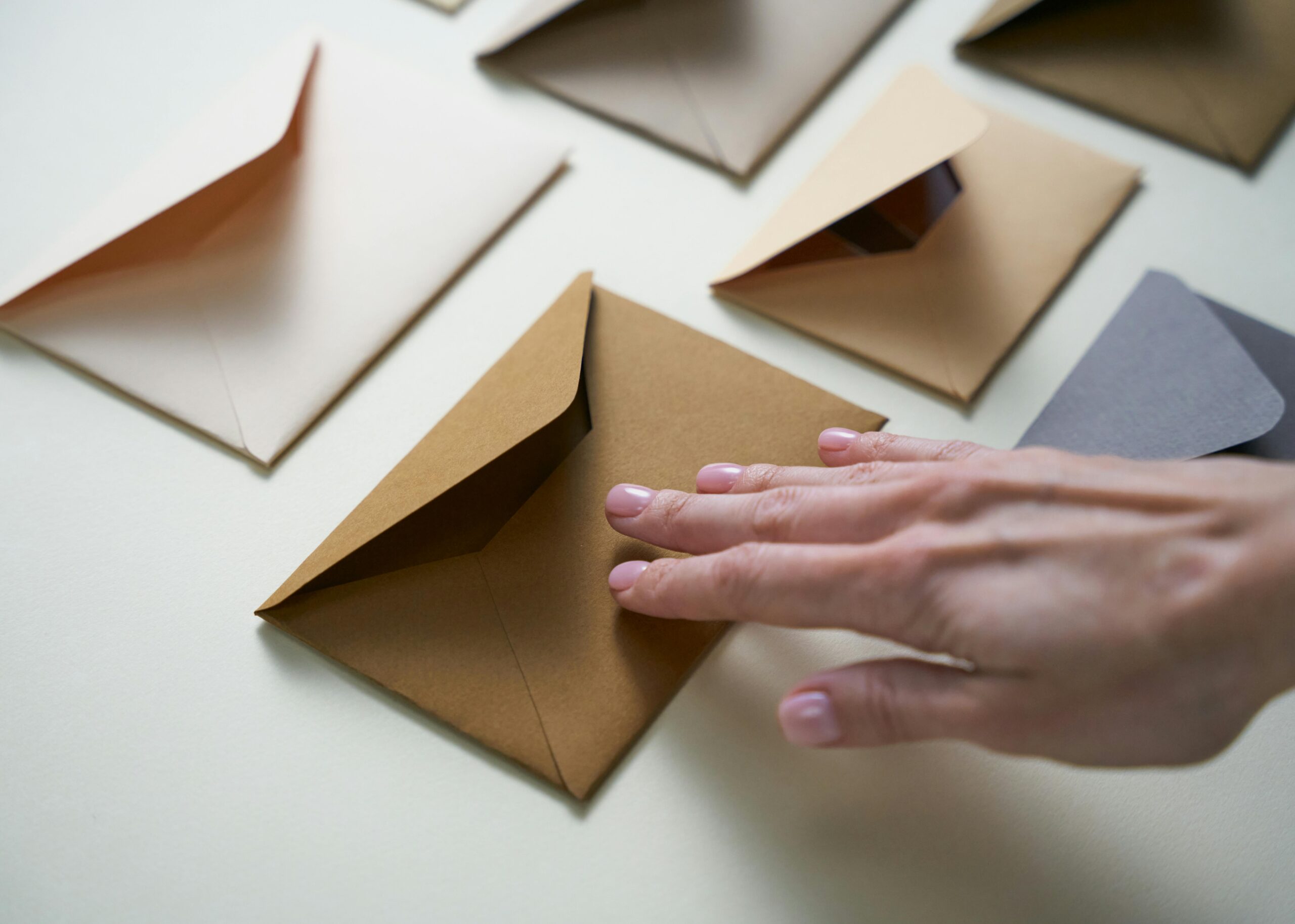 A hand gently touches brown envelopes spread on a white surface, illustrating organization.